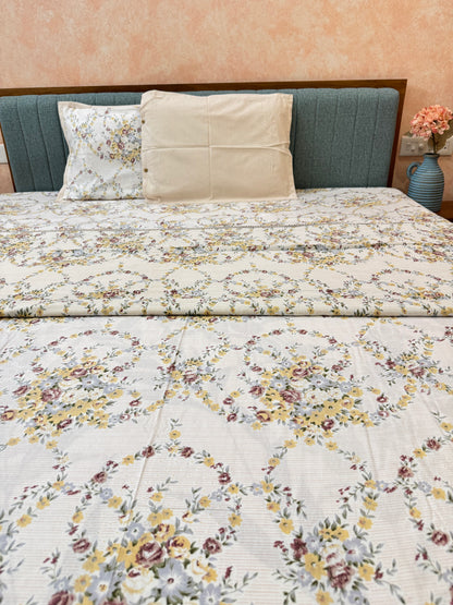 Floral patterned quilt on a bed with pillows against a pink wall.